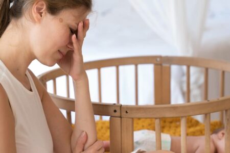 Jeune maman en post-partum, visage fatigué, bébé en arrière-plan.